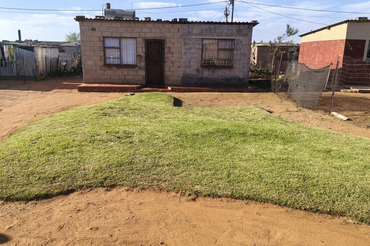 Front view of a single-story brick house featuring a solar water heater and a small front lawn area.