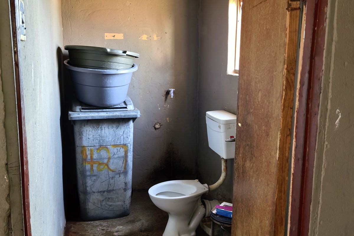 A small, basic bathroom featuring a toilet and exposed plumbing, requiring significant renovation and cosmetic updates to improve its condition and functionality.