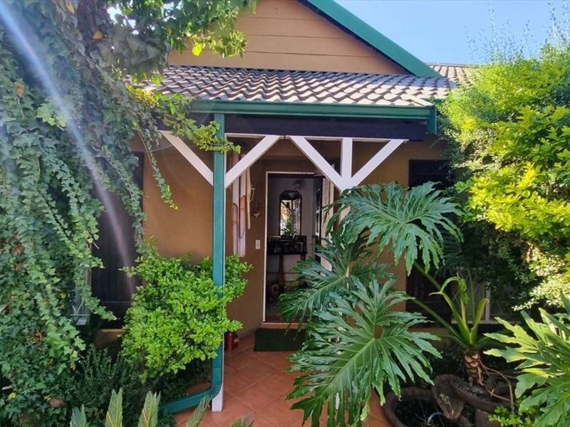 Front entrance of the house featuring a covered tiled porch with timber support posts, surrounded by established garden foliage.