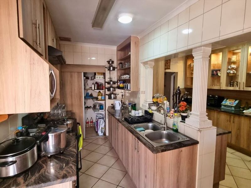 A functional kitchen featuring wood-look laminate cabinetry, granite countertops, a double basin sink, and a convenient walk-in pantry with tiled flooring throughout.