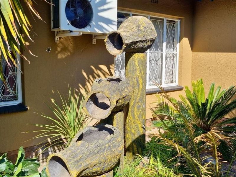 A garden area featuring a decorative water feature, exterior wall-mounted air conditioning unit, and security-barred windows.