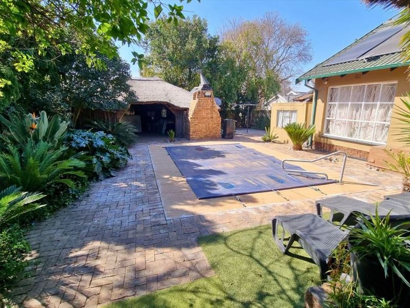 Outdoor pool area featuring a covered swimming pool, brick paving, and a traditional thatched lapa with a built-in brick braai.