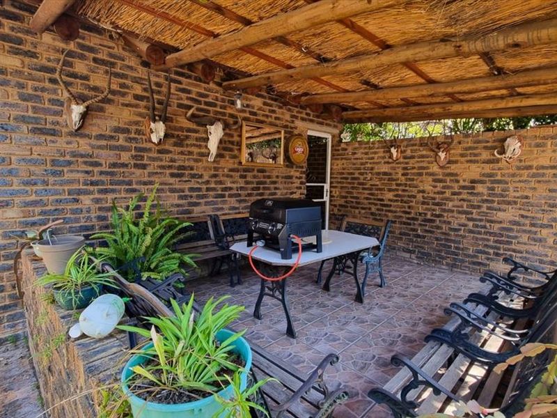 A covered outdoor patio area featuring a rustic thatched roof, exposed brick walls, and tiled flooring, suitable for outdoor entertaining.