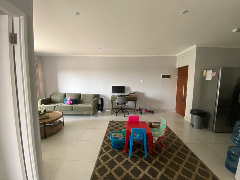 Spacious open-plan living area featuring neutral tiled flooring, recessed downlighting, and a solid wood entrance door.