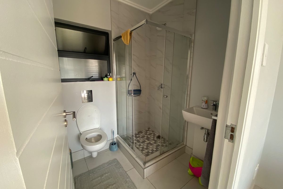 A compact bathroom featuring a glass shower enclosure, wall-mounted toilet, and pedestal basin with neutral floor and wall tiling.