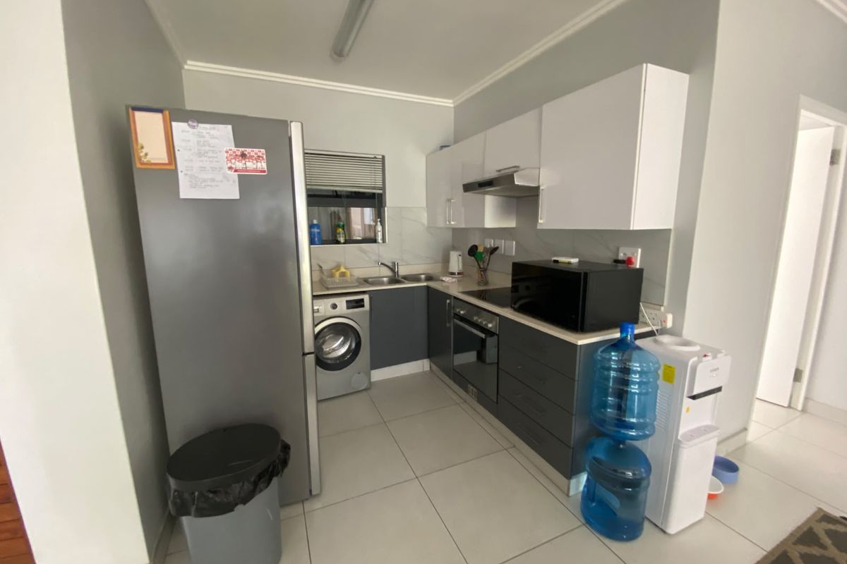 Compact kitchen featuring modern grey and white cabinetry, integrated appliances, tiled flooring, and a functional layout with a built-in oven and hob.