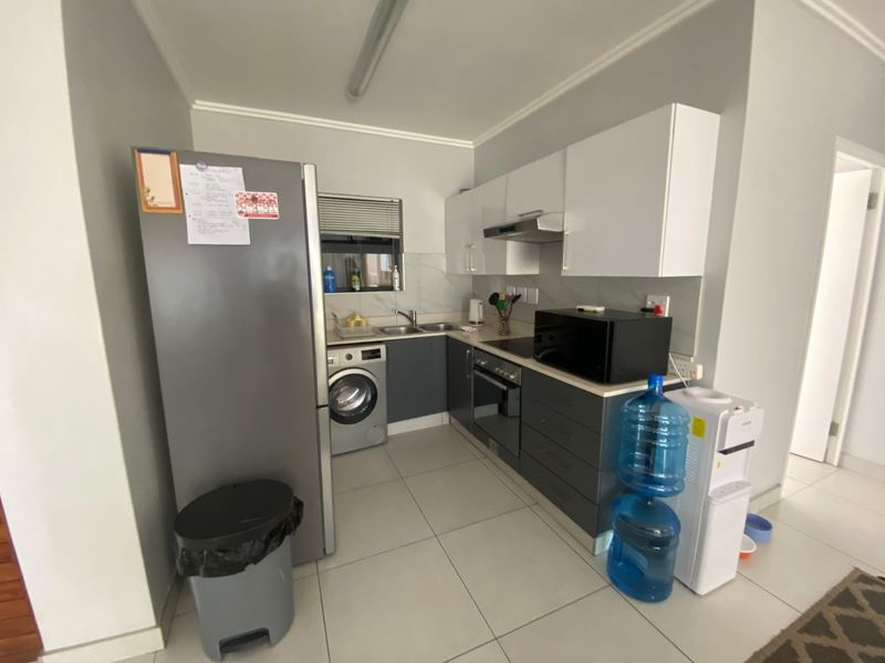 Compact kitchen featuring modern grey and white cabinetry, integrated appliances, tiled flooring, and a functional layout with a built-in oven and hob.