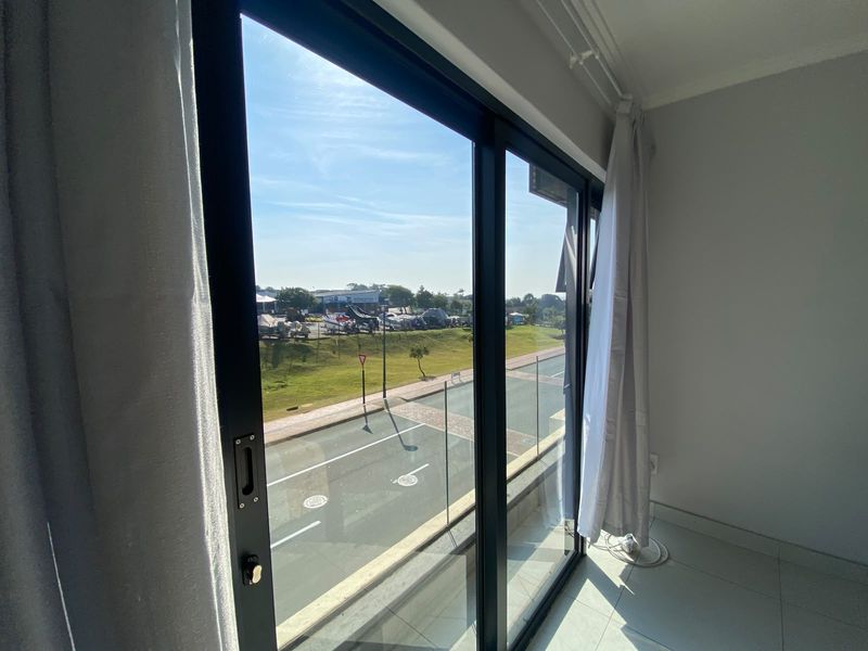 A view from an interior space through a large sliding glass door, overlooking a street and landscaped area.
