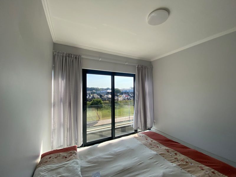 A bright bedroom featuring a sliding glass door that opens onto a balcony with a glass balustrade and exterior views.