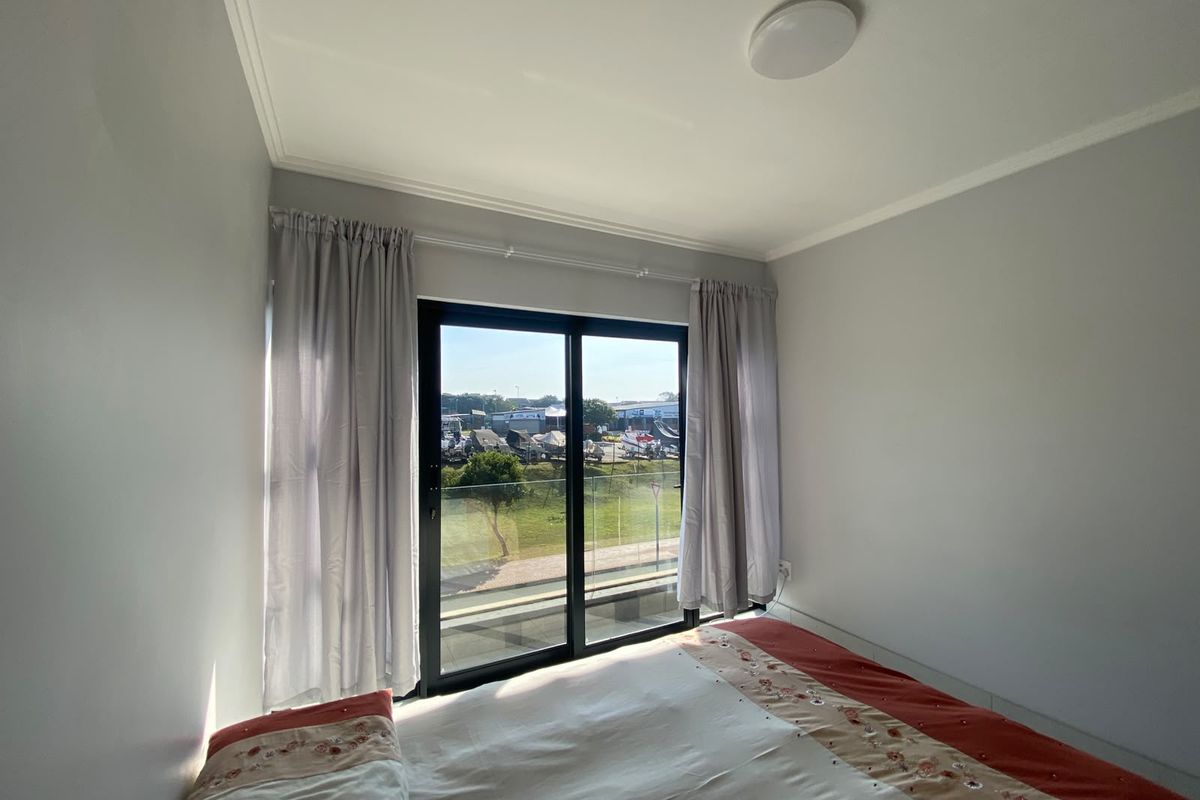 A bright bedroom featuring a sliding glass door that opens onto a balcony with a glass balustrade and exterior views.