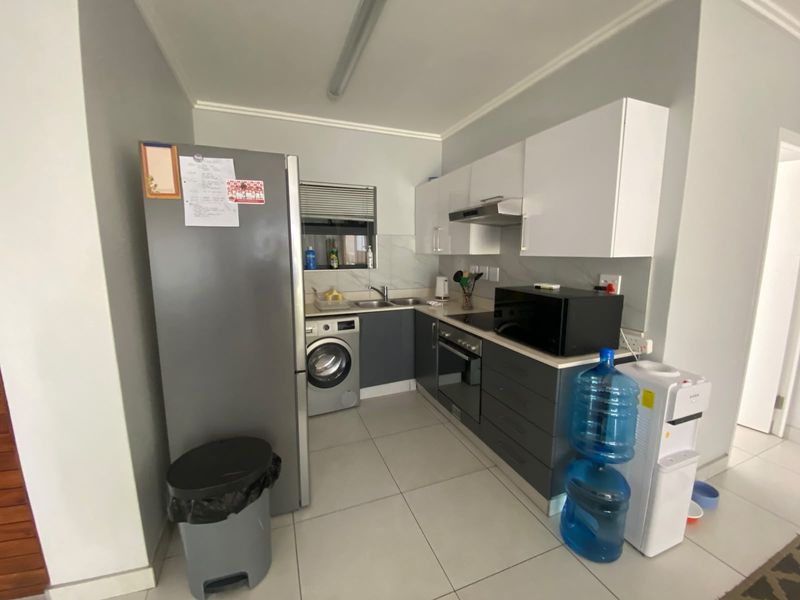 Compact kitchen featuring modern grey and white cabinetry, built-in oven, hob, extractor fan, and tiled flooring with integrated laundry plumbing.