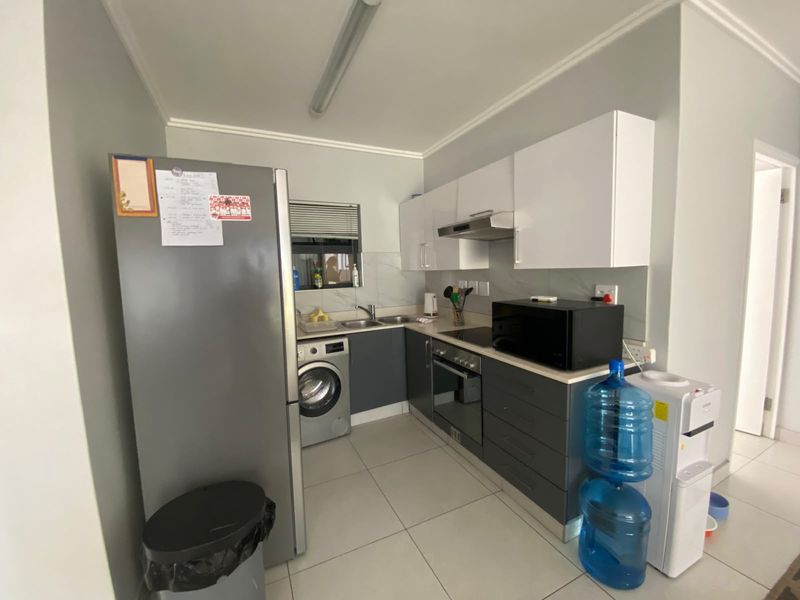 Compact modern kitchen featuring grey and white cabinetry, integrated appliances, marble-look splashback, and tiled flooring.