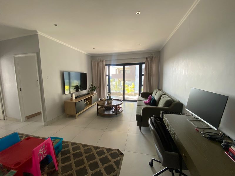 A bright living room featuring tiled flooring, recessed downlights, and a large sliding glass door providing access to the balcony.