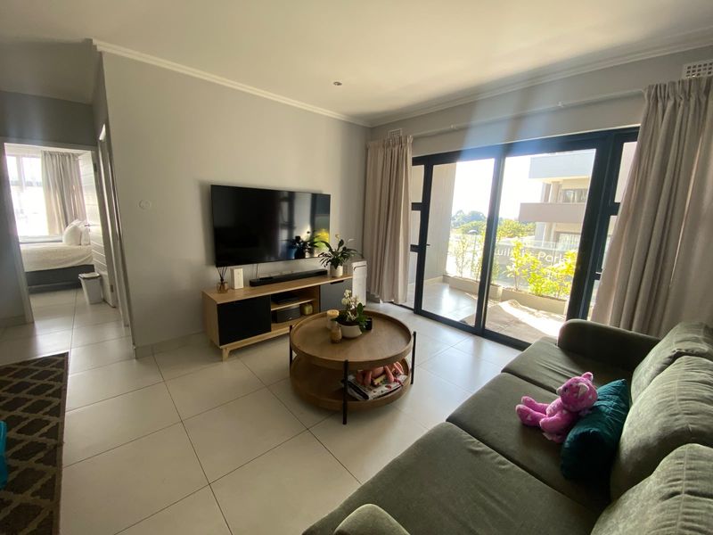 A bright living room featuring large sliding glass doors leading to a balcony, neutral tiled flooring, and modern recessed lighting.
