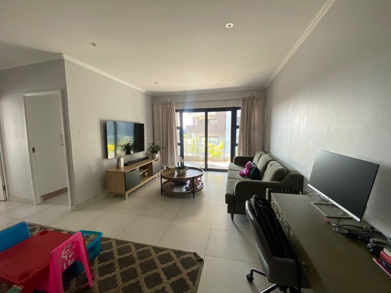 Spacious living room featuring neutral tiled flooring, recessed lighting, and large sliding glass doors providing access to the balcony.