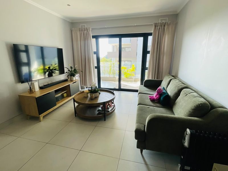 A bright and modern living room featuring large format floor tiles and a sliding glass door providing direct access to the balcony.