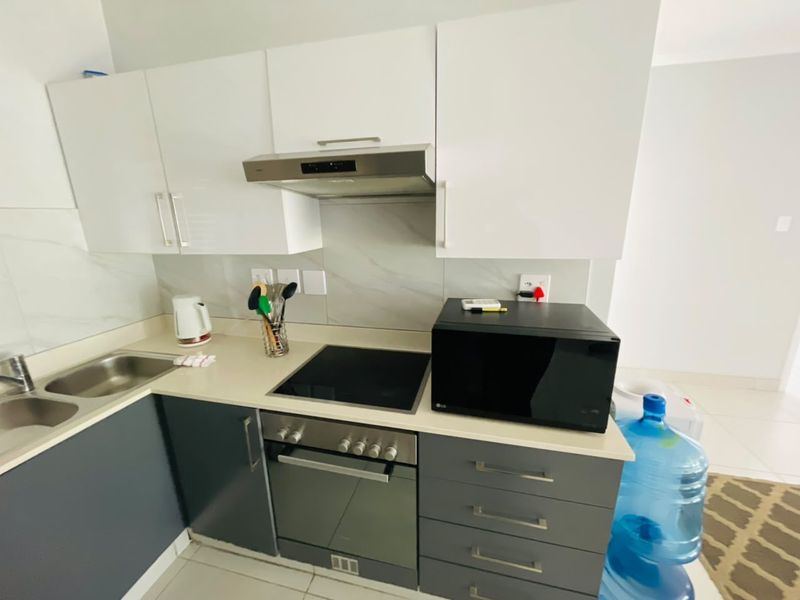 Modern kitchen featuring sleek white and grey cabinetry, stone countertops, integrated stainless steel oven, electric hob, and a tiled backsplash.