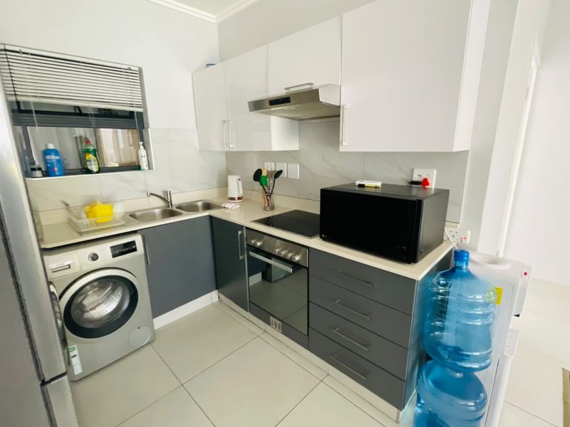 Modern kitchen featuring sleek grey and white cabinetry, integrated stainless steel appliances, tiled backsplash, and functional layout with built-in laundry connection.