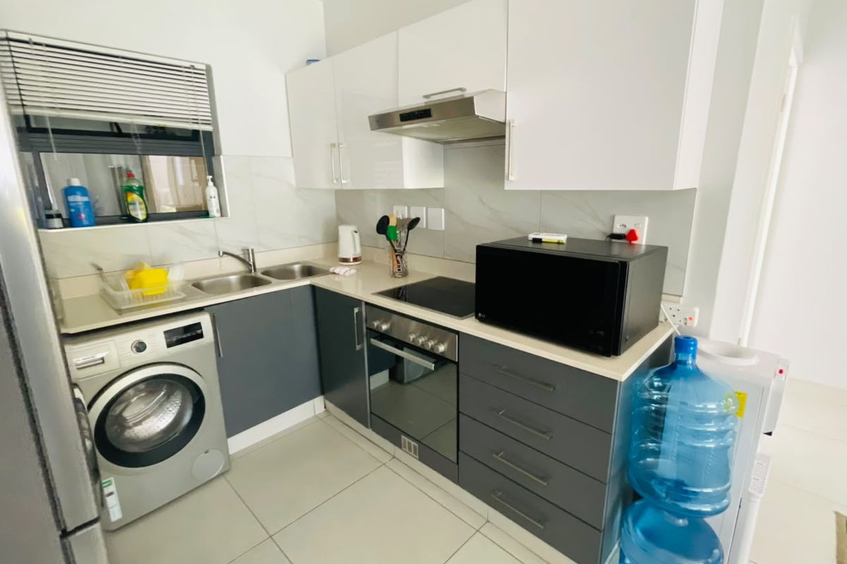Modern kitchen featuring sleek grey and white cabinetry, integrated stainless steel appliances, tiled backsplash, and functional layout with built-in laundry connection.
