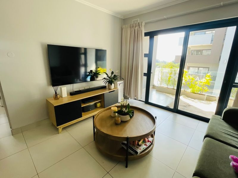 A bright living room featuring large sliding glass doors that open onto a balcony, with neutral tiled flooring and clean wall finishes.
