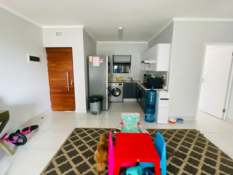 Open-plan living area featuring a compact kitchen with built-in cabinetry, tiled flooring, and direct access to a wooden entrance door.