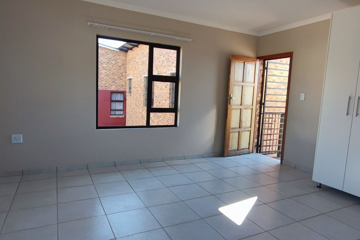 A bright, empty bedroom featuring neutral walls, tiled flooring, and a built-in wardrobe, with direct access to an exterior balcony area.