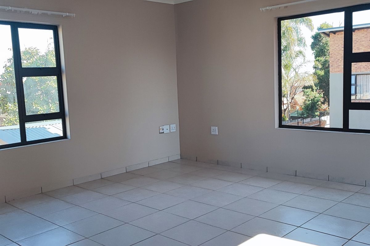 A bright, empty living area featuring neutral wall tones, tiled flooring, and large aluminium-framed windows providing natural light.