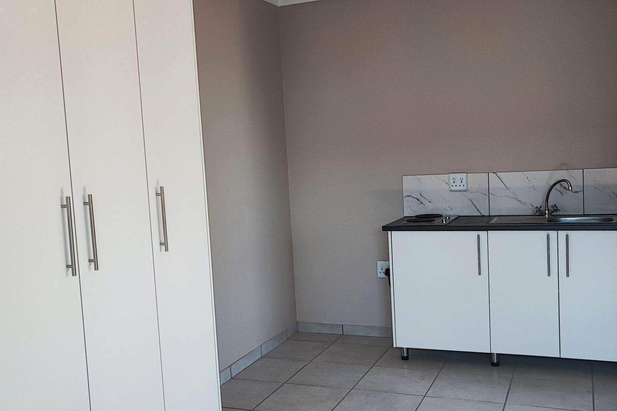 A compact kitchenette featuring white built-in cabinetry, a sink, and a marble-look splashback, adjacent to a large built-in wardrobe unit.