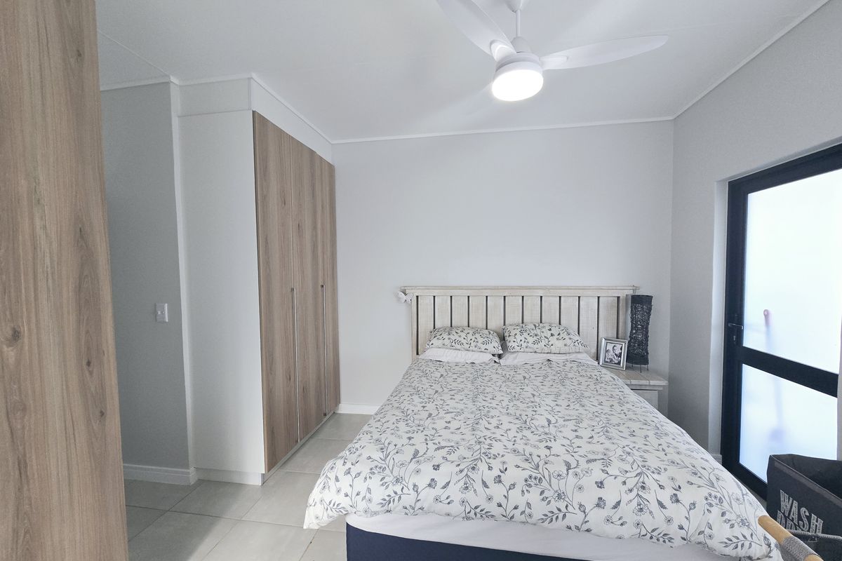 A well-maintained bedroom featuring built-in wood-finish cupboards, a modern ceiling fan, tiled flooring, and a glass panel door providing natural light.