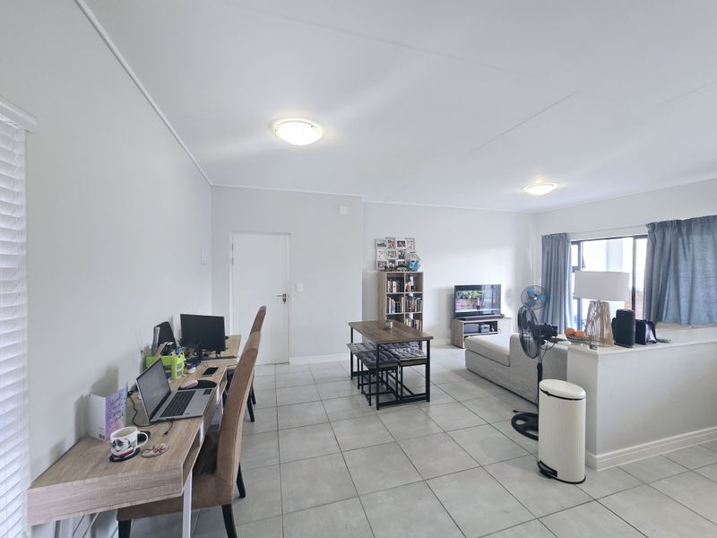 Spacious open-plan living area featuring neutral tiled flooring, clean white walls, and a functional layout connecting the living space to a dedicated work area.