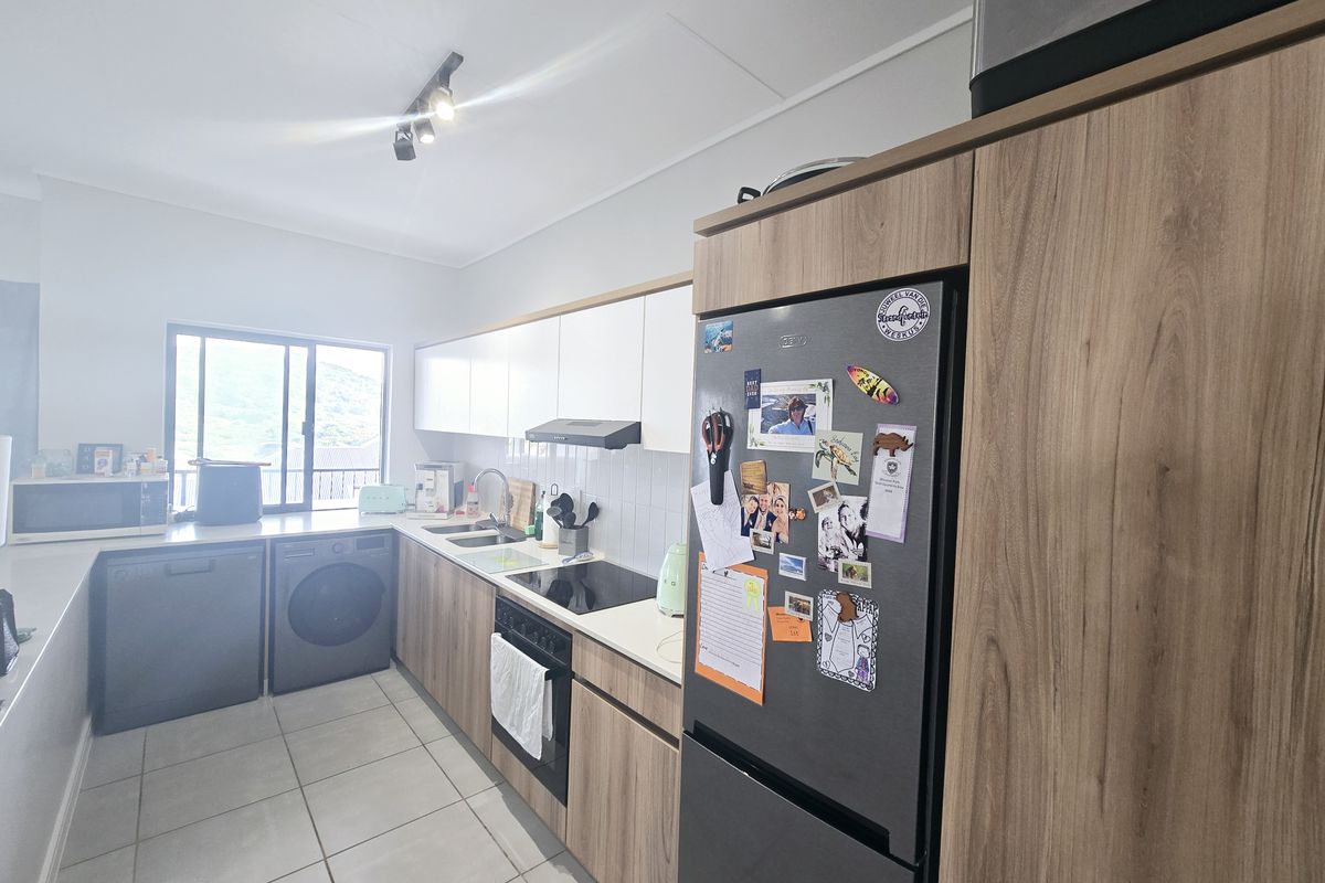 Modern kitchen featuring wood-grain cabinetry, white upper cabinets, integrated appliances, tiled flooring, and a functional layout with ample counter space.