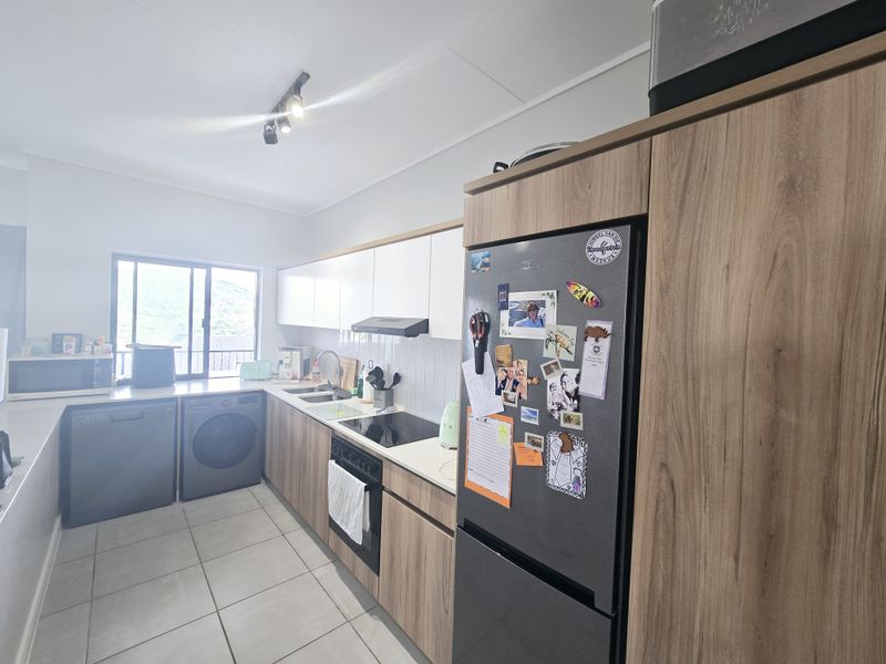 Modern kitchen featuring wood-grain cabinetry, white upper cabinets, integrated appliances, tiled flooring, and a functional layout with ample counter space.