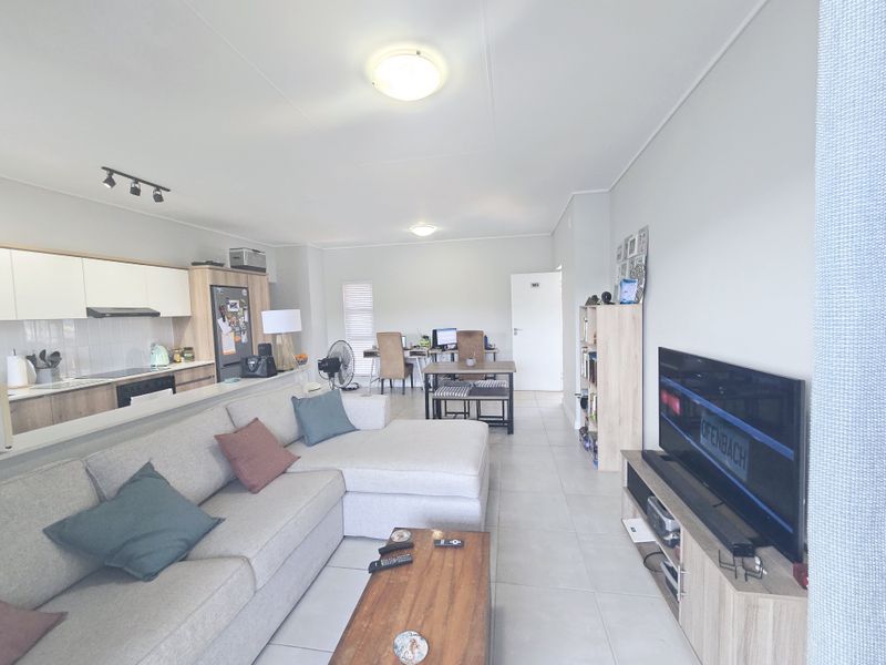 An open-plan living and kitchen area featuring tiled flooring, modern cabinetry, and integrated kitchen appliances in a well-maintained apartment setting.