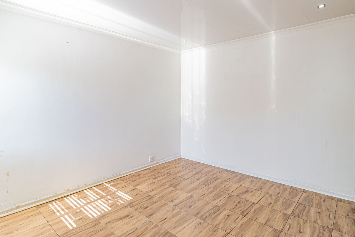 A bright, empty bedroom featuring wood-look tiled flooring, recessed ceiling lighting, and neutral white walls, providing a clean canvas for personalization.