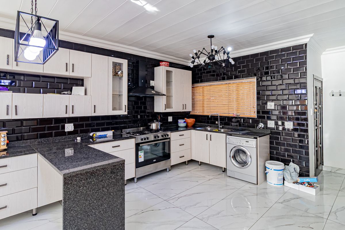 Modern kitchen featuring granite countertops, black subway tile backsplash, built-in oven with gas hob, and integrated laundry facilities.