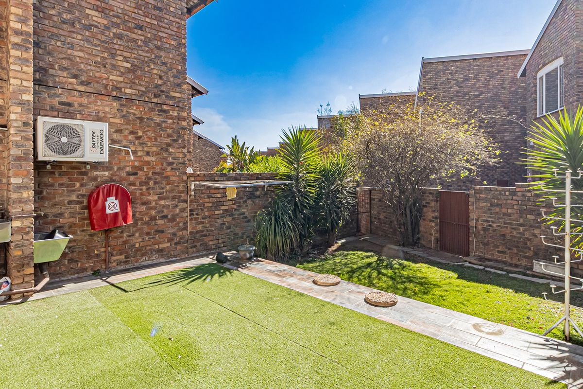 A private rear courtyard featuring face brick walls, artificial lawn, paved pathway, and utility fixtures including an air conditioning unit and fire hose reel.