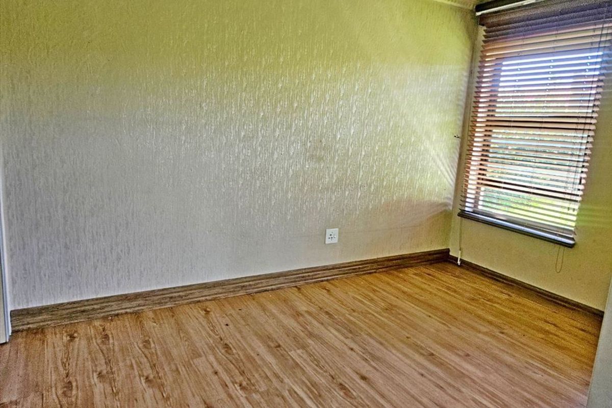 An empty bedroom featuring laminate flooring, textured wallpaper, and venetian blinds, providing a neutral canvas for personalization.