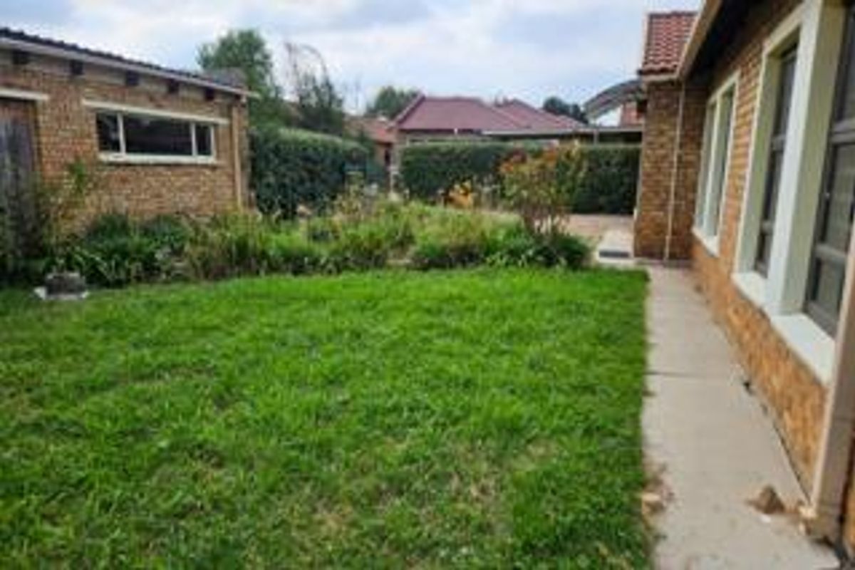 A rear garden view featuring a lawn, established hedging, and a concrete walkway alongside the face brick townhouse structure.