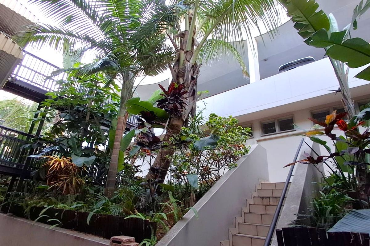 A view of the apartment building's rear exterior, featuring a concrete staircase, landscaped garden area, and elevated balconies.