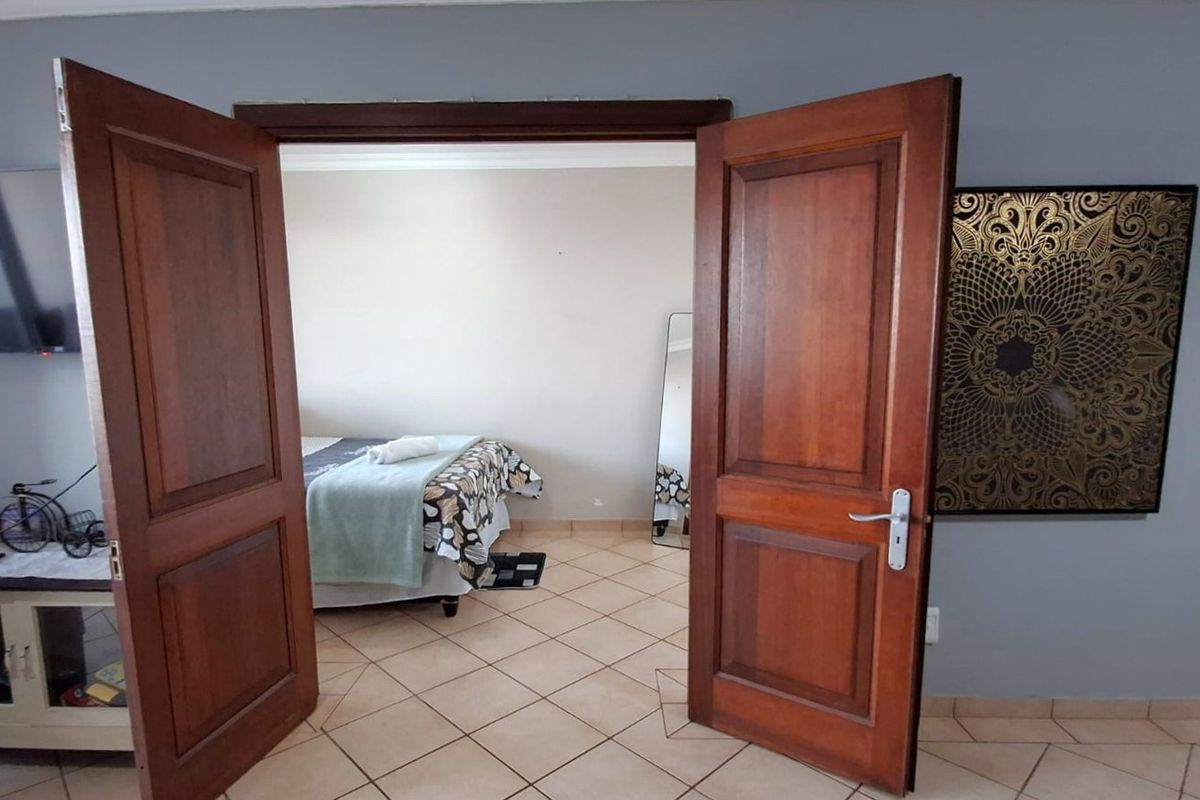 A bedroom accessed through double wooden doors, featuring ceramic tiled flooring and neutral wall finishes.