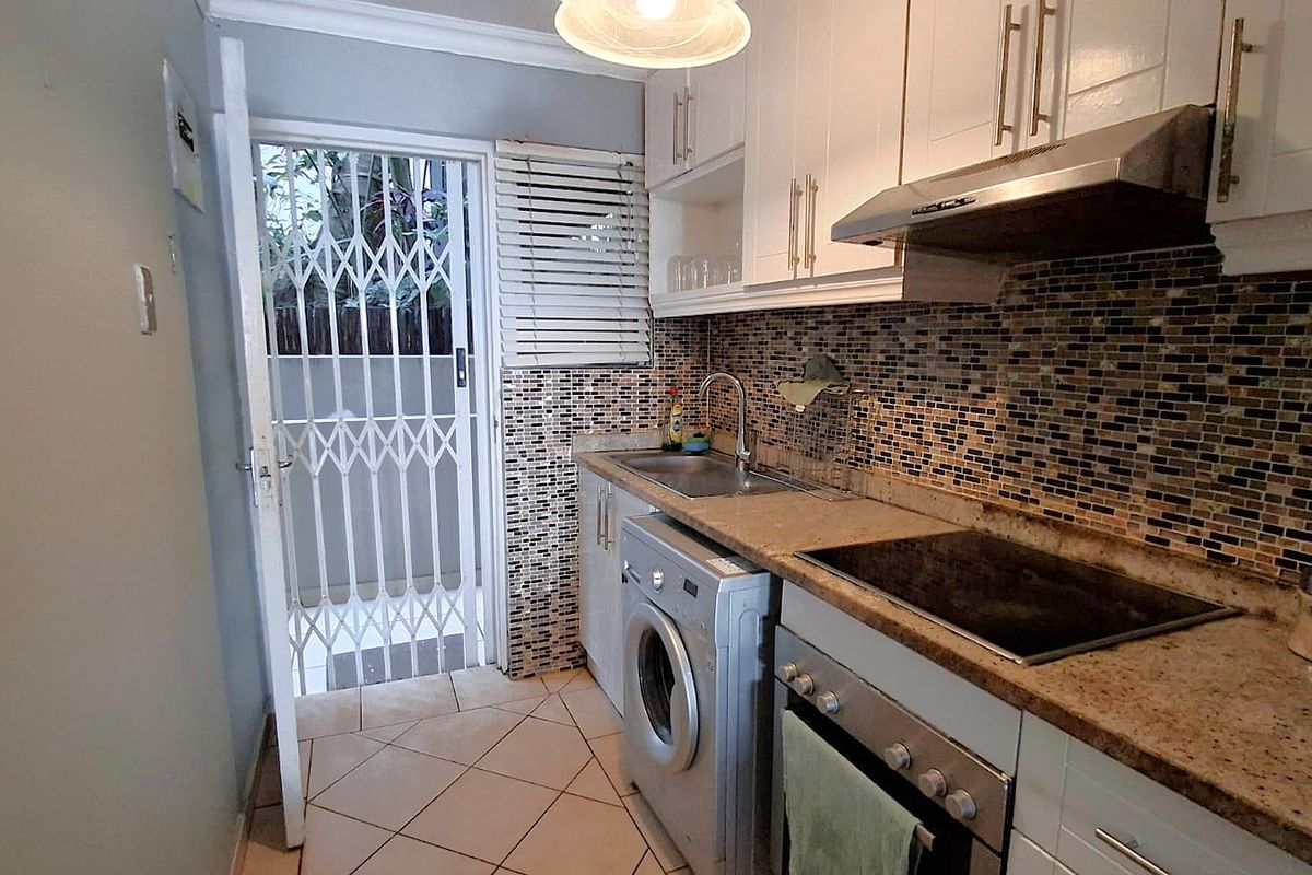 Compact kitchen featuring stone countertops, mosaic tile backsplash, built-in oven with hob, extractor fan, and direct access to an outdoor area via a security gate.