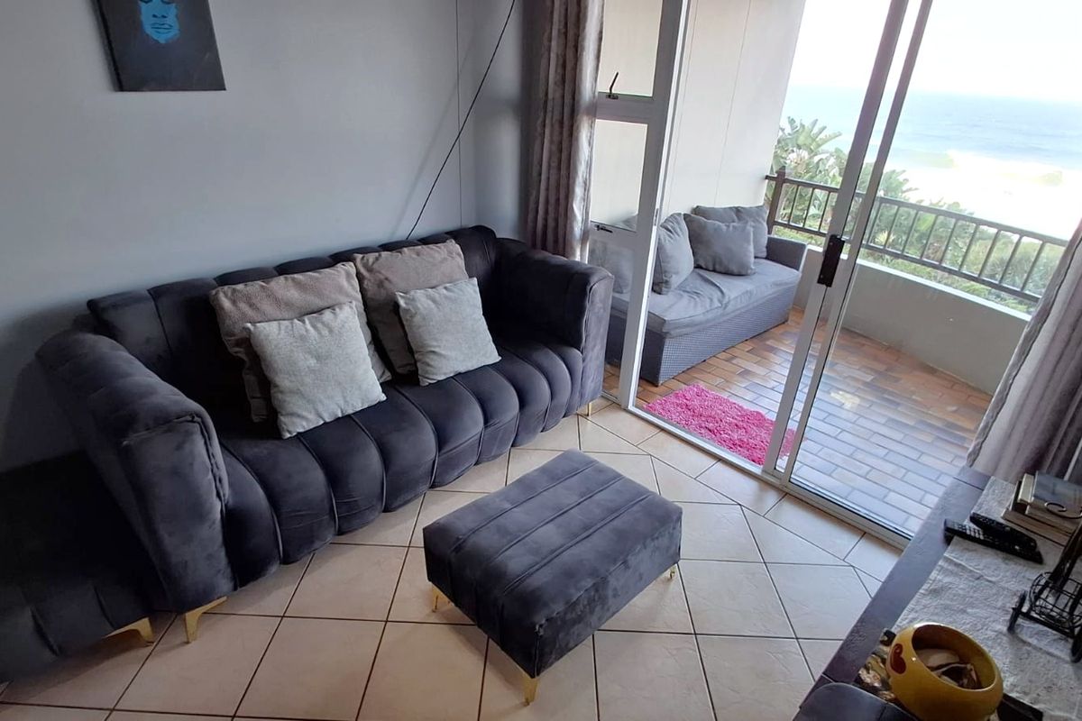 A living room featuring tiled flooring and large sliding glass doors that provide direct access to an outdoor balcony with ocean views.