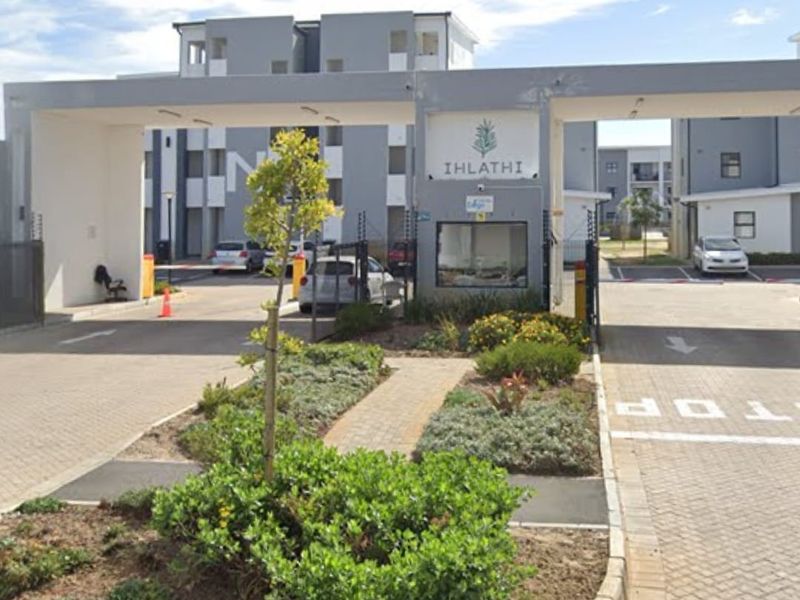The main entrance and security gatehouse of the Ihlathi apartment complex, featuring paved driveways and landscaped garden beds.