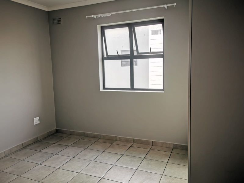 A clean, empty bedroom featuring neutral grey walls, tiled flooring, and an aluminium-framed window with a fitted curtain rail.