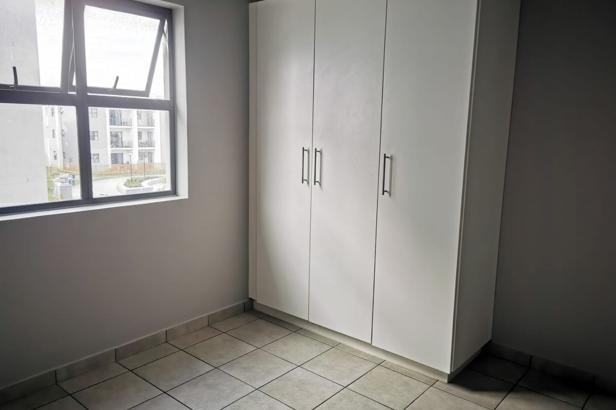 A clean, empty bedroom featuring neutral tiled flooring, a large built-in wardrobe, and a window providing natural light.
