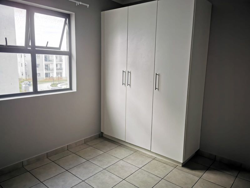 A clean, empty bedroom featuring neutral tiled flooring, a large built-in wardrobe, and a window providing natural light.