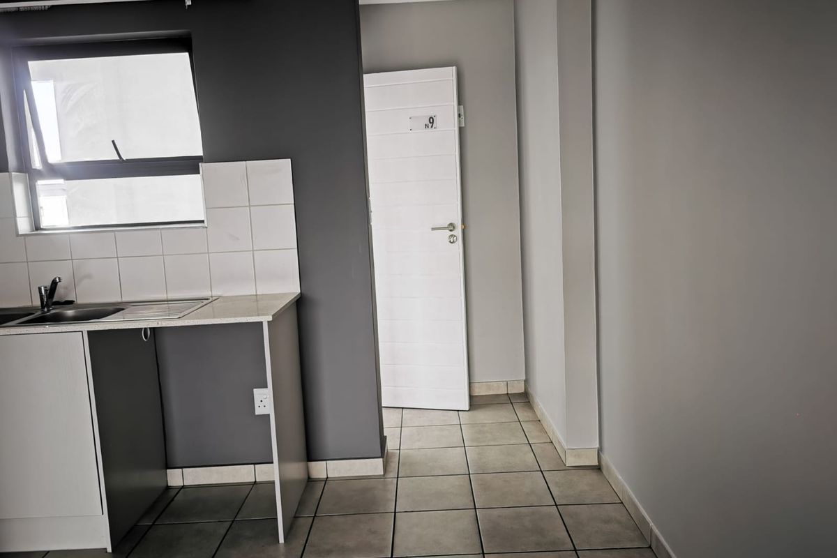 A compact kitchen area featuring tiled flooring, a sink with a tiled splashback, and neutral grey wall finishes.