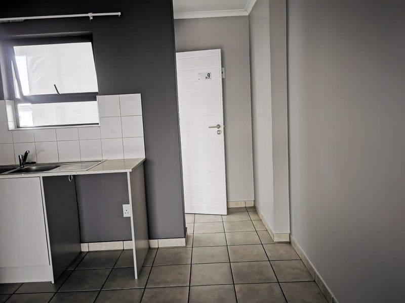 A compact kitchen area featuring tiled flooring, a sink with a tiled splashback, and neutral grey wall finishes.