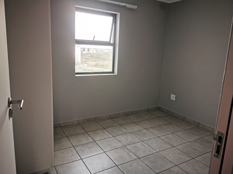 A clean, empty bedroom featuring neutral grey walls, tiled flooring, and a built-in cupboard, offering a blank canvas for personalization.