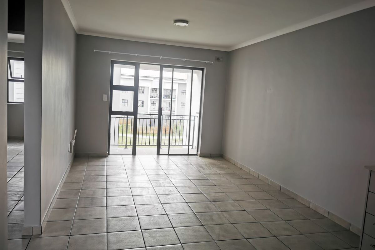An empty, open-plan living area featuring neutral grey walls, tiled flooring, and a sliding glass door providing access to a balcony.